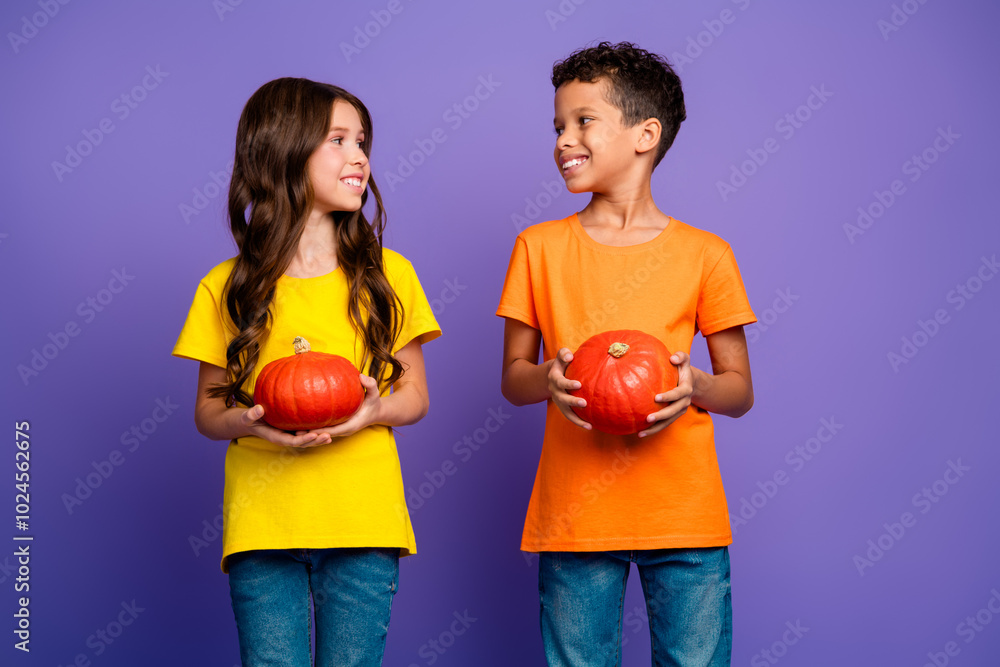 Poster Photo of charming two little children hold pumpkins look each other wear trendy orange yellow outfit isolated on violet color background