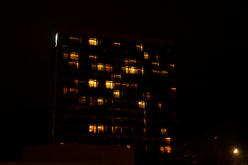 An indistinct image depicting a tall building featuring numerous windows that are illuminated...