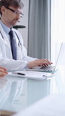 Male physician in white coat focused on laptop data in a modern clinic office while analyzing patient information on laptop. Medicine concept