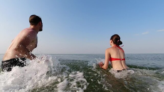 A young couple enjoys the first day of their holiday on the sea coast. Slow motion. Water games. Vacation and recreation