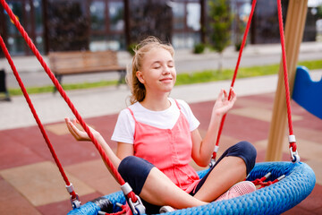 White-haired girl 10 years old playing, swings and slides on the playground in the summer in the city