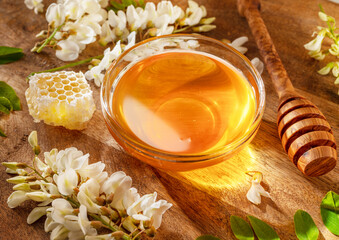 Natural organic honey in glass bowl, honey plant acacia flowers and leaves near it on wooden table. Top view.