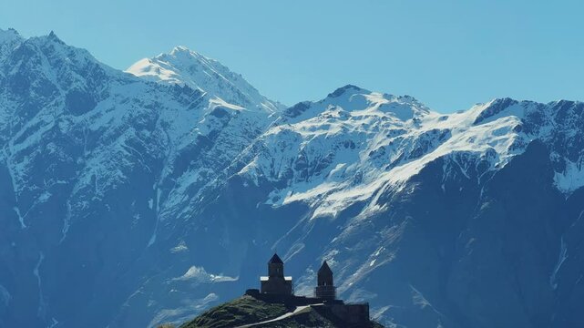 Trinity Church of Gergeti on the background of snow-capped mountains. View of the mountain peaks near Stepantsminda, Georgia. The ancient Christian church of Gergeti at the foot of Mount Kazbek. 4К