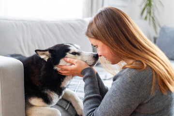 Woman touching noses with husky dog on sofa.