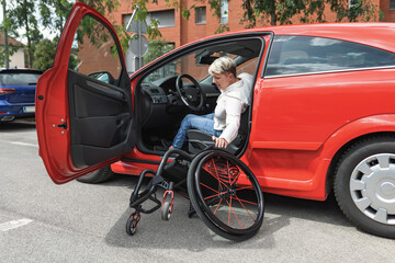 Fototapeta premium Female driver with physical impairment getting out from car and transferring into the wheelchair. Disability and mobility concept.