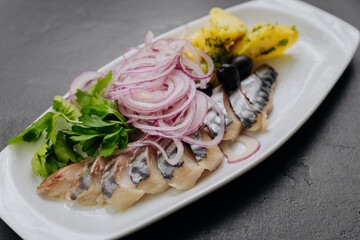 Traditional marinated herring with onion, potatoes and herbs on plate. Perfect for seafood lovers