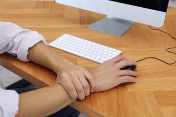 Man suffering from pain in wrist while using computer mouse at table indoors, closeup. Carpal...
