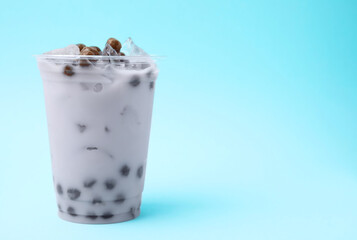 Tasty milk bubble tea in plastic cup on light blue background, space for text