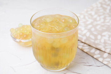 Tasty bubble tea in glass and tapioca pearls on white table, closeup