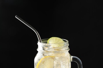 Tasty refreshing drink with straw in mason jar on dark background, closeup