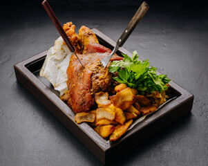 Juicy roasted pork knuckle served with herbs and vegetables on a dark background