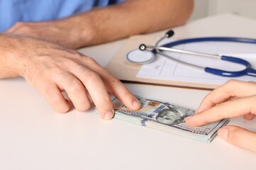 Corruption concept. Woman giving dollar banknotes to doctor at white table, closeup
