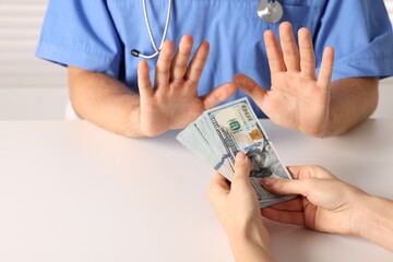 Corruption concept. Woman giving dollar banknotes to doctor at white table, closeup