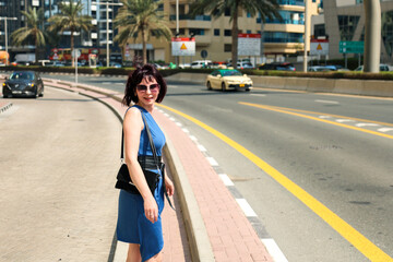 A woman in a summer dress walks along a busy road city.