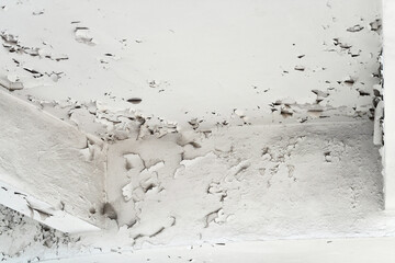 Close-up of peeling white paint on concrete stucco building balcony, exterior surface deterioration and urban decay. Selective focus.