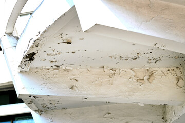 Aging stucco and cracked white paint on building's balcony, deterioration of exterior materials over time. Selective focus.