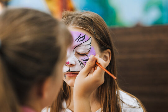 Professional make-up artist, female artist draws with pencil, brush, watercolors, makes face painting for a beautiful girl, child for Halloween. Photography, portrait.