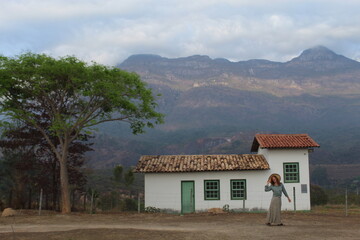 mulher caminhando ao lado de casa rústica com serra do caraça ao fundo, em catas altas, minas...