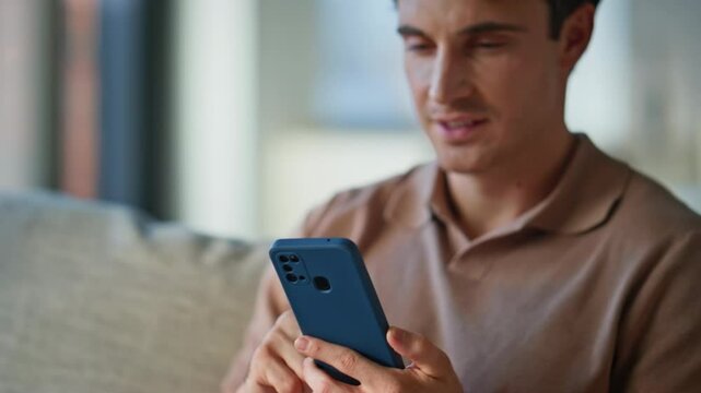 Cheerful guy looking smartphone on sofa modern apartment closeup. Smiling man