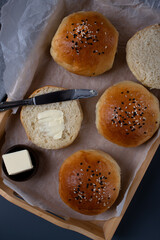 Yeast buns with sesame seeds on a wooden tray, served with butter. Top view