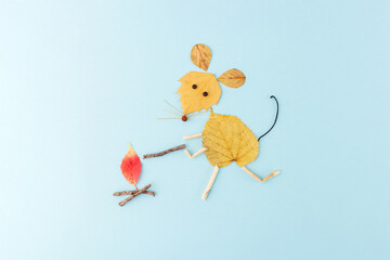 a creative and artistic composition of a mouse made from autumn leaves and twigs on a light blue background. red leaf that looks like a flame, use of natural elements ,