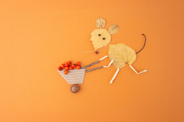 Autumn craft for kids, creative arrangement of leaves, twigs, and berries on orange background...