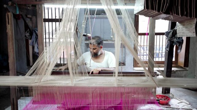 Indian mature man sitting at handloom weaving with purple thread