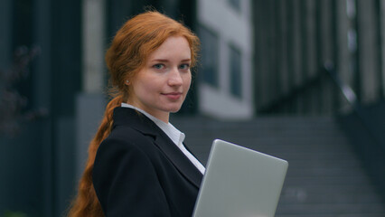 Happy smiling joyful Caucasian young female business woman girl employee CEO holding laptop device posing outside. Positive attractive businesswoman turning looking at camera wide smile outdoors city