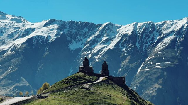 Trinity Church of Gergeti on the background of snow-capped mountains. View of the mountain peaks near Stepantsminda, Georgia. The ancient Christian church of Gergeti at the foot of Mount Kazbek. 4К
