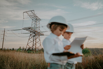 Little kids playing as engineers or managers with safety helmets, using tablet. Electrical industry profession, serious smart children on transmission power lines background.