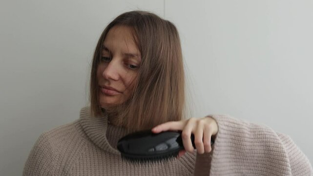 Young woman with static electricity on her natural short hair after combing hair with hairbrush on wall background. Girl with electrified hair. Staticky hair. Beauty treatment.