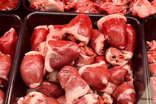 close up large red raw turkey hearts lie in black container at supermarket. offal . raw poultry meat