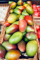 close in wicker brown baskets lies many mangoes next to pomegranate in supermarket. sale of products . juicy fruits
