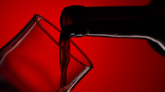 Wine. Pouring red wine into glass from the bottle on the black background. The camera moves around the bottle and glass of wine. Slow-motion shot in close-up