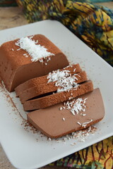 Dark chocolate milk pudding cake with cocoa powder and coconut flakes topping served on a plate. Selective focus