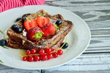 French toast crowned with vibrant strawberries, Red currant, blueberries and a fresh mint leaf, served with maple syrup, dusted delicately with powdered sugar