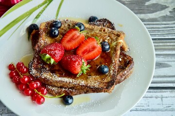 French toast crowned with vibrant strawberries, Red currant, blueberries and a fresh mint leaf, served with maple syrup, dusted delicately with powdered sugar