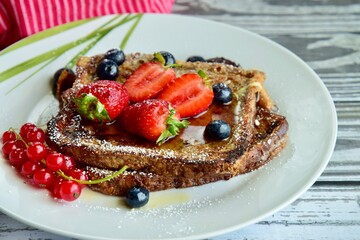 French toast crowned with vibrant strawberries, Red currant, blueberries and a fresh mint leaf, served with maple syrup, dusted delicately with powdered sugar