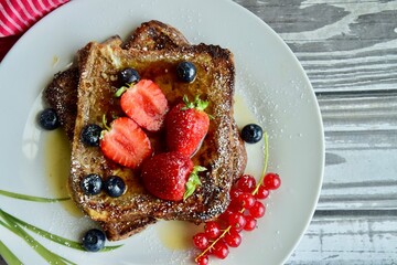 French toast crowned with vibrant strawberries, Red currant, blueberries and a fresh mint leaf, served with maple syrup, dusted delicately with powdered sugar