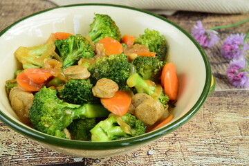 Stir fried broccoli with carrot and chicken sausage in a ceramic dish on wooden table. homemade style food concept.