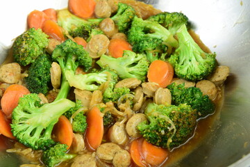 Stir fried broccoli with carrot and chicken sausage in a wok on wooden table. homemade style food concept.