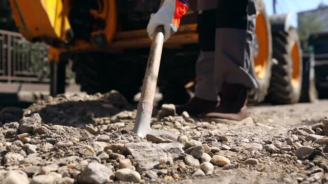 Workers are fixing a damaged road surface in a bustling downtown area, using shovels and heavy machinery to prepare the ground for repair.