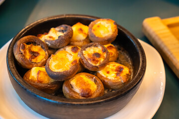 Delicious mushrooms stuffed with cheese baking in a clay pot, turning golden brown and crispy, creating a mouthwatering appetizer. Aroma fills the kitchen, promising a tasty meal