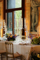 Modern luxury destination wedding decor in dark gold mode in historical Italian villa Arvedi with candelabras, gold chairs flowers and artworks