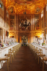 Modern luxury destination wedding decor in dark gold mode in historical Italian villa Arvedi with candelabras, gold chairs flowers and artworks