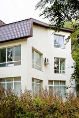 A modern three-story house covered with white plaster and a brown metal roof.
