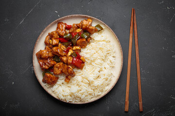 Steaming Chinese kung pao chicken with rice, veggies, and peanuts in spicy sauce. Top view on dark background. Perfect for lunch or dinner