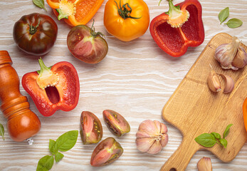Colorful bell peppers, tomatoes, pepper mill, basil, garlic arranged beautifully on a white wooden table, creating a rustic kitchen scene with space for text. Food and diet concepts