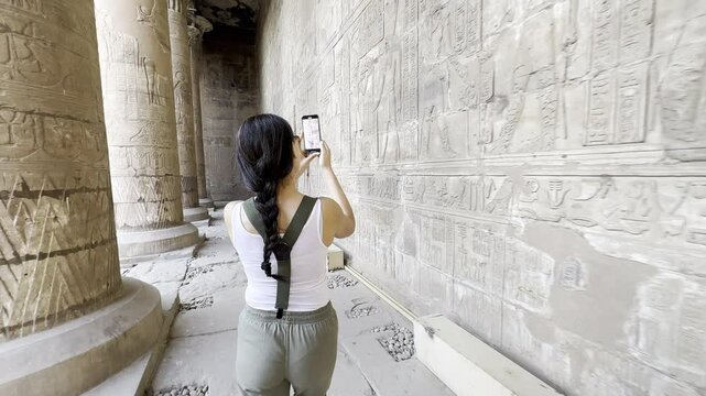 Tourist capturing ancient Egypt with your camera as you explore the magnificent Temple of Horus at Edfu. Recording his journey through this historic site with his phone to share.