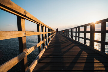 The planked passage to the lighthouse on the seashore during the golden hour at dawn